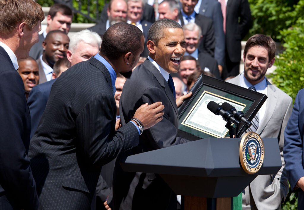 President Barack Obama receives a share of Packers stock from Charles Woodson as Aaron Rodgers looks on.